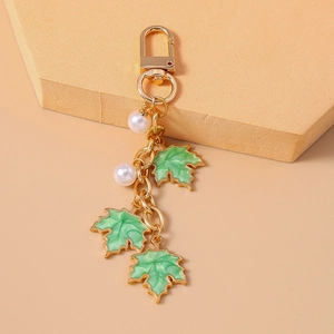 Detail of green maple leaf charms with white pearls on a gold metal keychain link