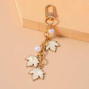 Detail of gold maple leaf keychain with white enamel pendants and faux pearls on hooks