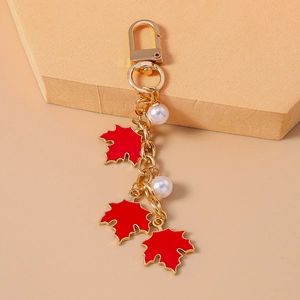 Close-up of red maple leaf keychain with white pearls on a soft pink background