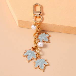 Detail of golden keychain with light blue maple leaves and elegant white pearls