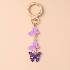 Détail d'un porte-clés papillon doré avec émail lilas mat et pendentifs bleu-violet