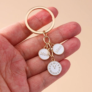 Porte-clés horloge Mom doré avec pendentifs en émail blanc sur un fond rose uni