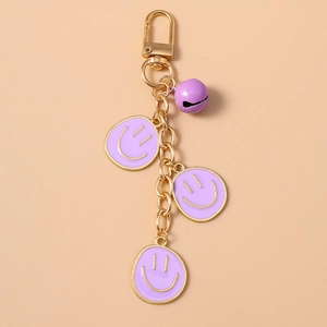 Dettaglio di ciondoli smiley in smalto viola e campanellino su portachiavi d'oro