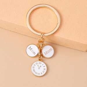 Détail de breloques dorées Mom et d'un pendentif horloge en émail blanc sur un porte-clés
