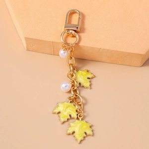 Detail of golden maple leaf keychain with yellow enamel charms and white imitation pearls