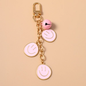 Dettaglio di moschettone dorato con campanellino rosa e ciondoli smiley su portachiavi