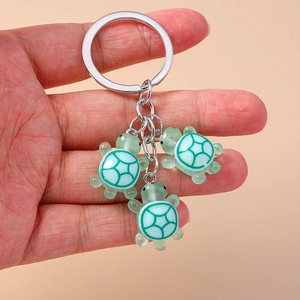 Détail d'un porte-clés triple tortue avec pendentifs en résine verte tenu à la main