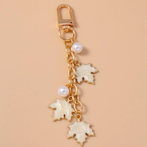Close-up of golden maple leaf keychain with white pearls and cream enamel charms on pink background