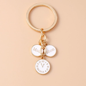 Détail d'un porte-clés horloge doré avec breloques Mom sur un fond de couleur pastel