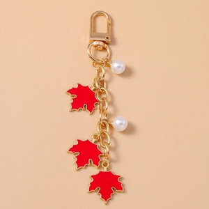 Detailed close-up of golden maple leaf keychain with red enamel and white pearls