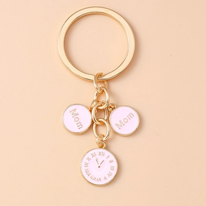 Détail du porte-clés doré avec pendentifs Mom en émail rose et breloque horloge chic