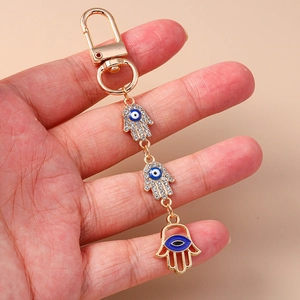 Golden Evil Eye and Hamsa Hand keychain with blue rhinestones held in hand