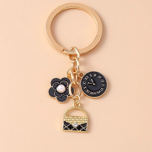 Close-up of golden keychain with black camellia flower, clock charm and quilted bag detail