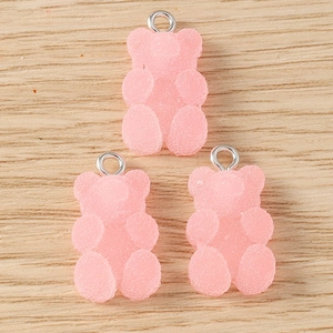 Close-up of three pink resin gummy bear pendants with silver rings on wood surface