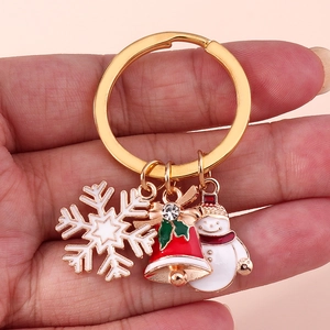 Christmas snowman and red bell charms on golden keychain held against pink background