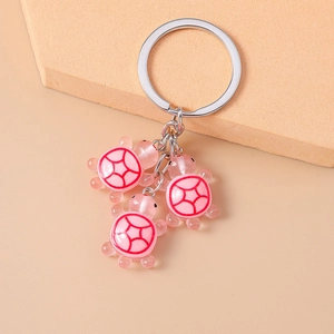 Détail de trois breloques tortue en résine rose attachées à un porte-clés en argent