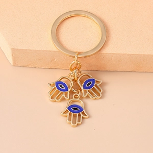 Detail eines goldenen Hamsa-Hand-Schlüsselanhängers mit blauen Evil-Eye-Anhängern auf beige