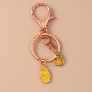 Détail d'un porte-clés en or rose avec breloques banane et bouteille de lait émaillée