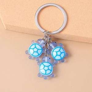 Détail de trois tortues en résine bleue avec motifs géométriques sur un porte-clés argenté