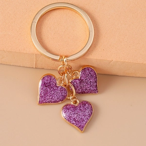 Detail of gold keychain featuring three heart pendants with sparkling purple glitter finish
