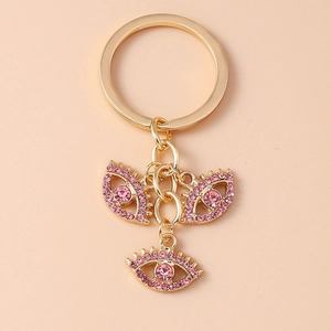 Detail eines goldenen Schlüsselanhängers mit drei rosa Evil Eye-Anhängern und Kristallen