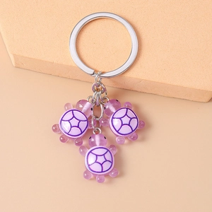 Détails de mignons porte-clés tortues en résine violette sur un fond de couleur rose pastel