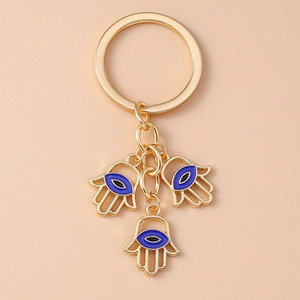 Detail der goldenen Hamsa-Hand Schlüsselanhänger mit blauen Evil-Eye-Anhängern auf Rosa