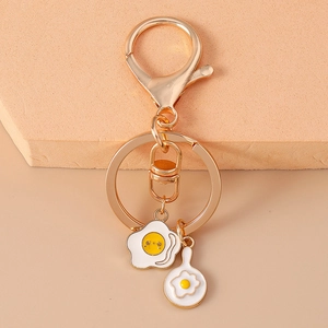 Close-up of golden cartoon fried egg and frying pan charms on a metal keychain