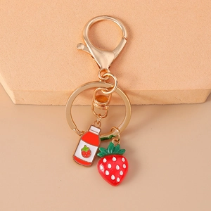 Close-up of golden keychain with strawberry juice bottle and red berry enamel charms