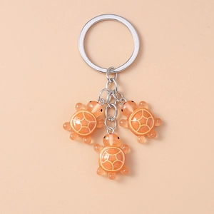 Vue détaillée de trois tortues en résine orange sur un porte-clés argenté avec motifs de carapace