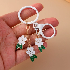 Detailed view of hand holding white cherry blossom keychain with enamel flowers and gold chain