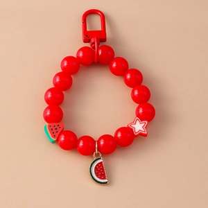 Detail of red beaded keychain featuring watermelon charm and star pendant on pink background