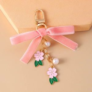 Portachiavi elegante con fiocco in velluto rosa, fiori dorati e perle su sfondo caldo