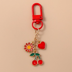 Detail of red cherry, daisy, and heart enamel charms on a golden metal keychain link