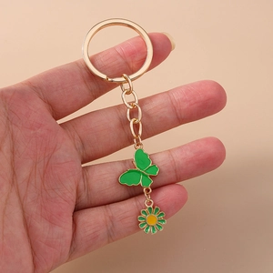 Détail du porte-clés doré avec pendentif papillon en émail vert et fleur de marguerite