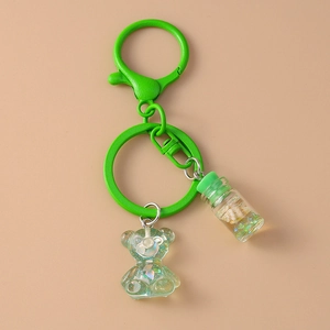 Detail of green metallic key ring with transparent resin bear and ocean bottle charm
