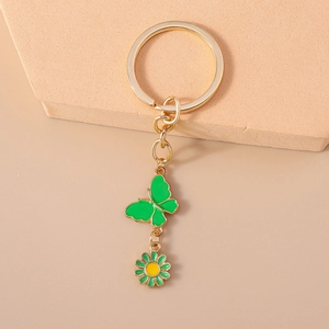 Vue détaillée d'un porte-clés doré avec pendentifs papillon vert et marguerite fleurie