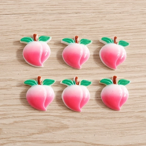 Detailed view of six resin peach charms with green leaves on light wood texture background