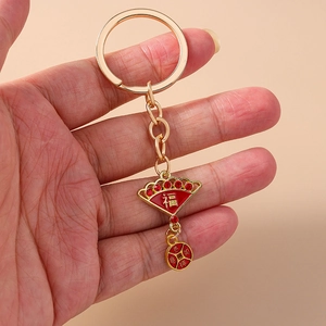 Detail of gold metal keychain with red enamel fan pendant and lucky fortune charms