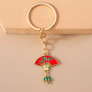 Detail of Chinese style red fan keychain with gold bamboo leaves on a warm stone background
