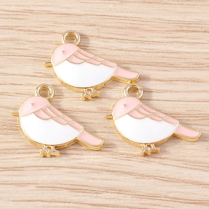 Detailed macro of three pink and white enamel bird pendants on light wood surface