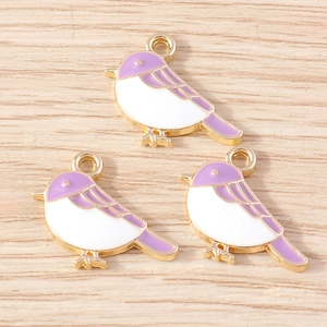 Detailed macro of three purple and white enamel bird charms with gold metal edges