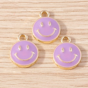 Three purple enamel smiley face charms with golden outlines on a light wood background