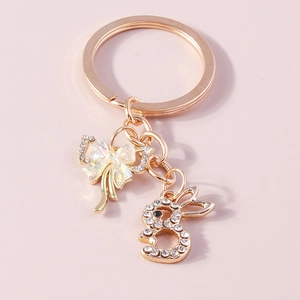 Golden bunny keychain with crystal bow and iridescent accents on pink background