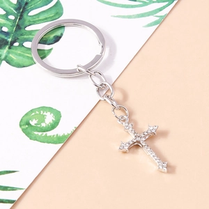 Porte-clés croix en métal argenté avec cristaux étincelants sur une surface rose pâle