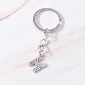 Close-up of silver letter H keychain with sparkling rhinestones on marble background