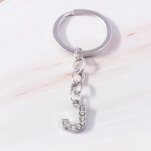 Detailed view of silver letter J keychain with sparkling rhinestone inlay and marble background
