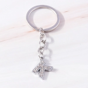 Detailed view of silver letter K keychain with sparkling rhinestones on marble surface