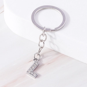 Detail shot of silver letter L keychain with sparkling rhinestones on stone background