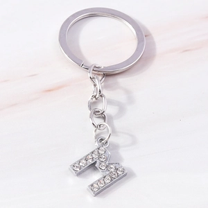 Close-up of a silver letter M keychain featuring sparkling rhinestones on marble background